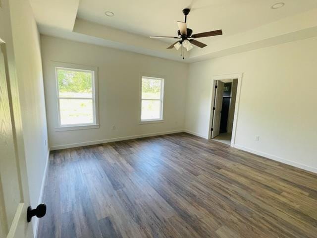 empty room with a tray ceiling, ceiling fan, and dark wood-type flooring