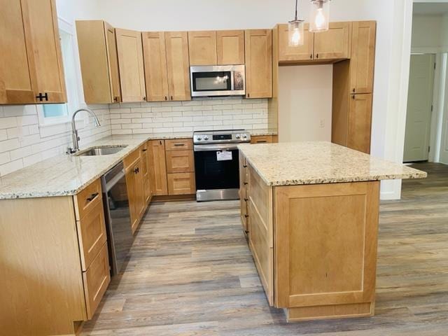 kitchen with sink, hanging light fixtures, stainless steel appliances, light hardwood / wood-style flooring, and a kitchen island