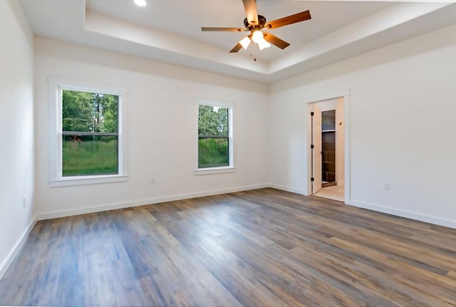 unfurnished room featuring a tray ceiling, ceiling fan, plenty of natural light, and dark hardwood / wood-style floors