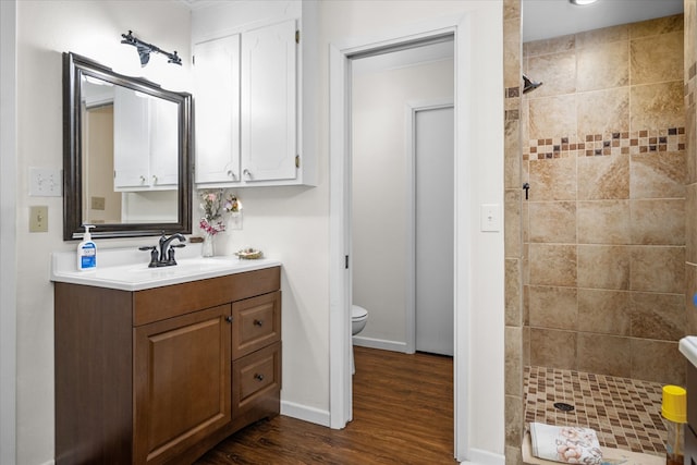 bathroom featuring a tile shower, vanity, toilet, and wood-type flooring