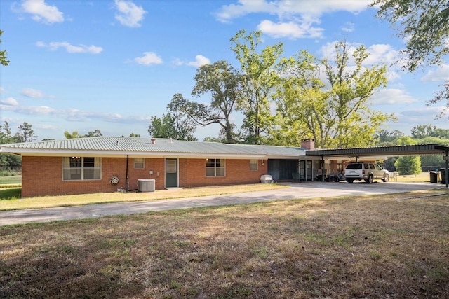 rear view of property with central air condition unit, a lawn, and a carport