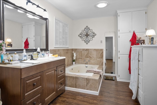 bathroom featuring hardwood / wood-style floors, vanity, a relaxing tiled tub, and ornamental molding