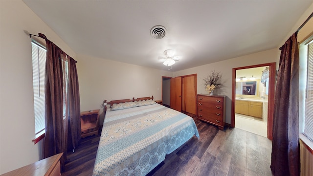 bedroom with connected bathroom, dark hardwood / wood-style flooring, and multiple windows