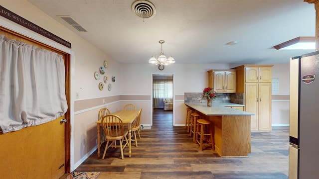 kitchen featuring a kitchen breakfast bar, light brown cabinetry, dark hardwood / wood-style flooring, kitchen peninsula, and stainless steel refrigerator