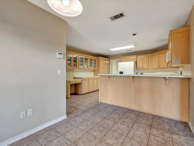 kitchen with kitchen peninsula, light brown cabinetry, white refrigerator with ice dispenser, and a breakfast bar area