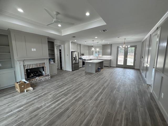 unfurnished living room with visible vents, dark wood-style flooring, crown molding, a raised ceiling, and a brick fireplace