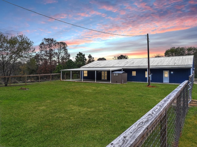 back house at dusk featuring an outbuilding and a yard