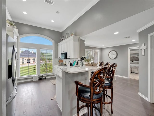 kitchen with hardwood / wood-style floors, white cabinets, kitchen peninsula, stainless steel fridge with ice dispenser, and a breakfast bar area