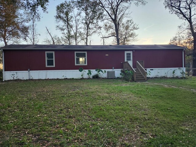 back house at dusk with a yard and central air condition unit