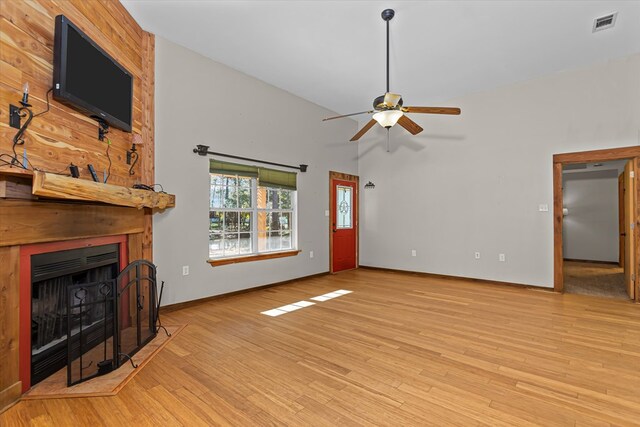 living room featuring ceiling fan, a large fireplace, light wood-type flooring, and a towering ceiling