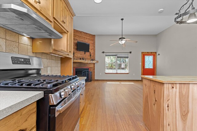 kitchen featuring decorative backsplash, light hardwood / wood-style floors, stainless steel gas range oven, and ceiling fan