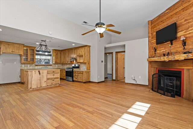 kitchen with a large fireplace, sink, stainless steel gas range oven, light hardwood / wood-style flooring, and decorative backsplash