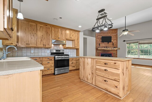 kitchen with backsplash, hanging light fixtures, sink, light wood-type flooring, and stainless steel range