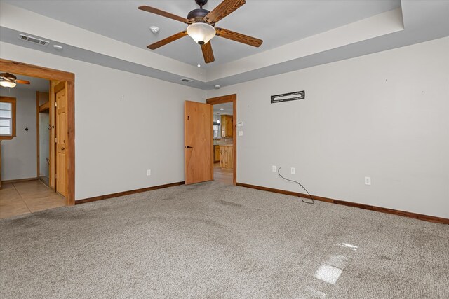 unfurnished room with a raised ceiling, ceiling fan, and light colored carpet