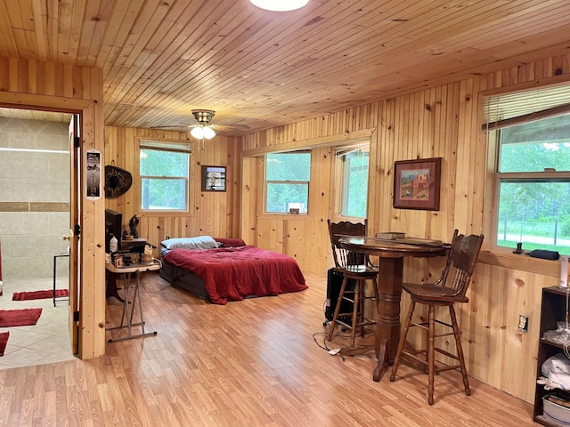 bedroom featuring light wood-type flooring, wood ceiling, ceiling fan, bar, and wood walls