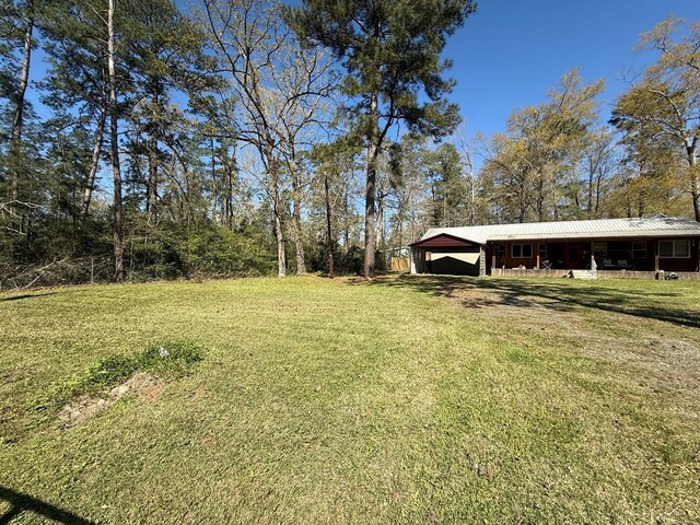 view of front of home featuring metal roof, covered porch, dirt driveway, a carport, and a front lawn