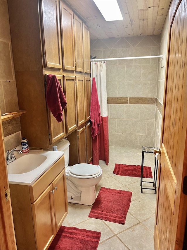 full bath featuring a skylight, toilet, vanity, tiled shower, and tile patterned floors