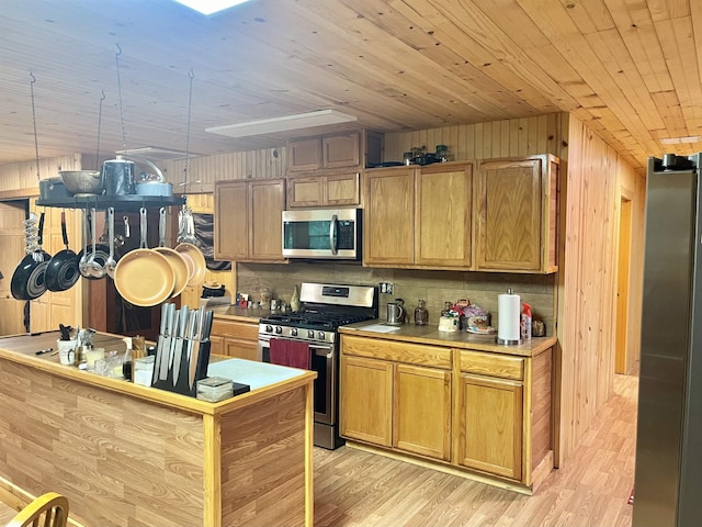 kitchen featuring wood walls, hanging light fixtures, light hardwood / wood-style flooring, tasteful backsplash, and stainless steel appliances