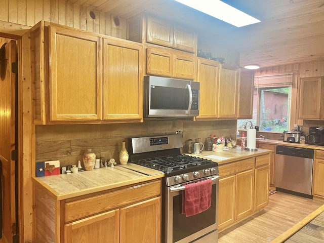 kitchen with light brown cabinetry, appliances with stainless steel finishes, a skylight, light wood finished floors, and light countertops