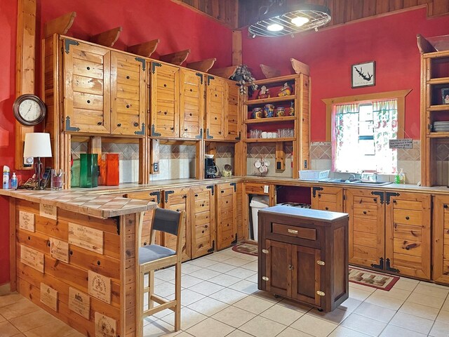 kitchen with light tile patterned flooring, decorative backsplash, a high ceiling, open shelves, and tile counters