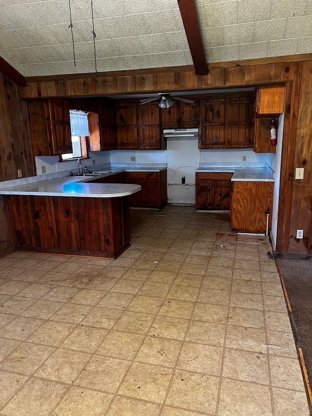 kitchen featuring kitchen peninsula, ceiling fan, wooden walls, sink, and beamed ceiling