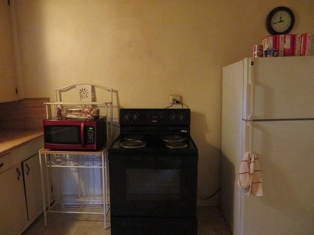 kitchen featuring black range with electric cooktop, white fridge, and white cabinets