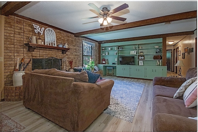 living room with light wood-type flooring, a brick fireplace, a textured ceiling, ceiling fan, and beam ceiling