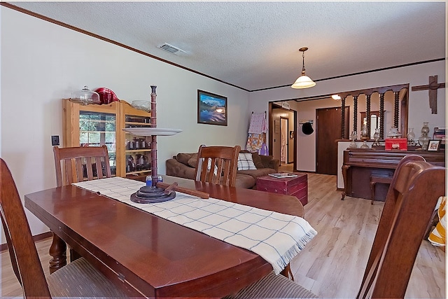 dining area with a textured ceiling, light hardwood / wood-style flooring, and ornamental molding