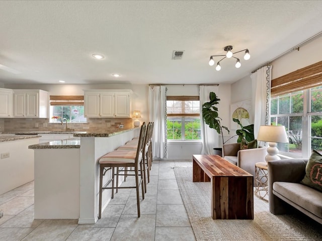 301 Sawgrass Cir, Lufkin, TX 75901 - kitchen with light stone countertops, backsplash, white cabinetry, a breakfast bar, and recessed lighting