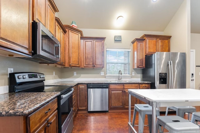 kitchen with a kitchen bar, stainless steel appliances, dark stone countertops, and sink