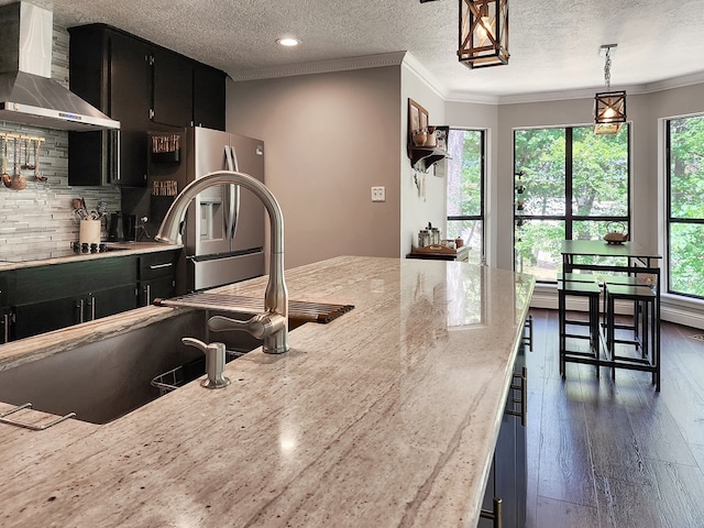 203 Bogey Ln, Brookeland, TX 75931 - kitchen with wall chimney exhaust hood, dark cabinetry, ornamental molding, light stone countertops, and a textured ceiling