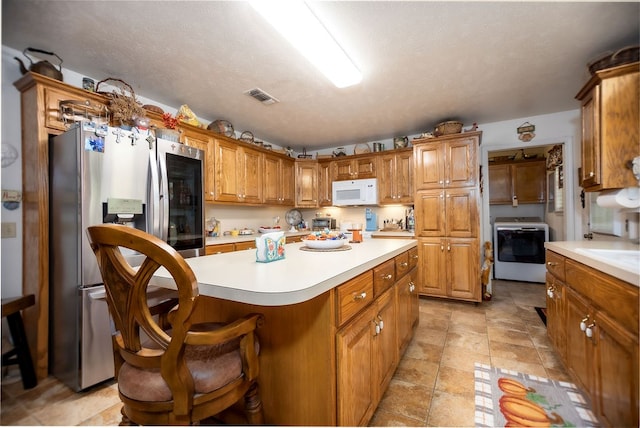 kitchen with a textured ceiling, a kitchen island, washer / dryer, stainless steel fridge with ice dispenser, and a breakfast bar area