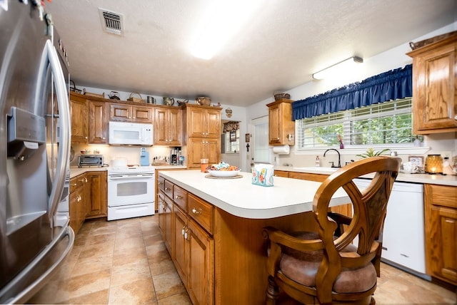 kitchen with white appliances, sink, a textured ceiling, a kitchen island, and a breakfast bar area