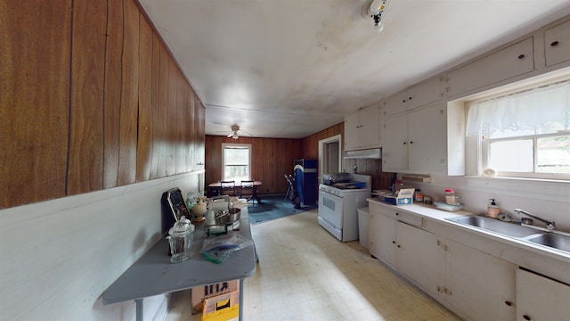 kitchen with white cabinetry, gas range gas stove, sink, ceiling fan, and wooden walls