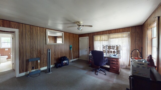 carpeted office space featuring ceiling fan and wooden walls