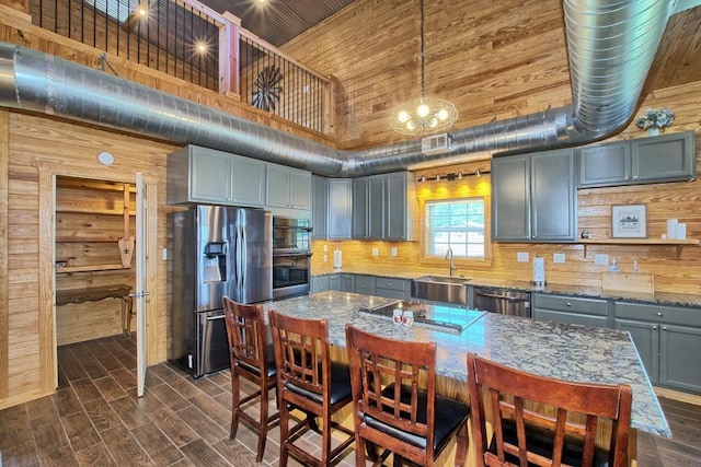 kitchen featuring wooden walls, pendant lighting, stainless steel appliances, and a high ceiling