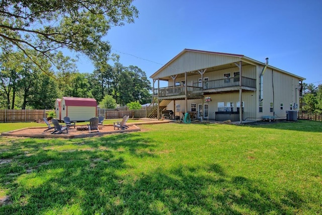 rear view of house with a yard, a fire pit, central air condition unit, a shed, and a patio area