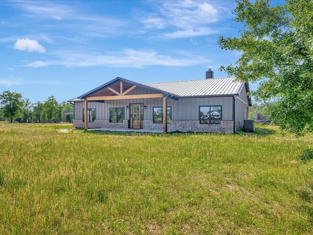 rear view of property featuring a chimney, central AC unit, board and batten siding, brick siding, and metal roof