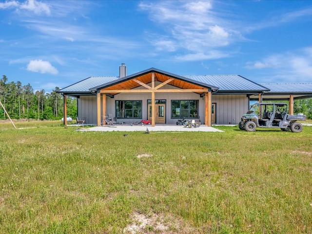 rear view of property featuring a chimney, a yard, a standing seam roof, a patio area, and metal roof