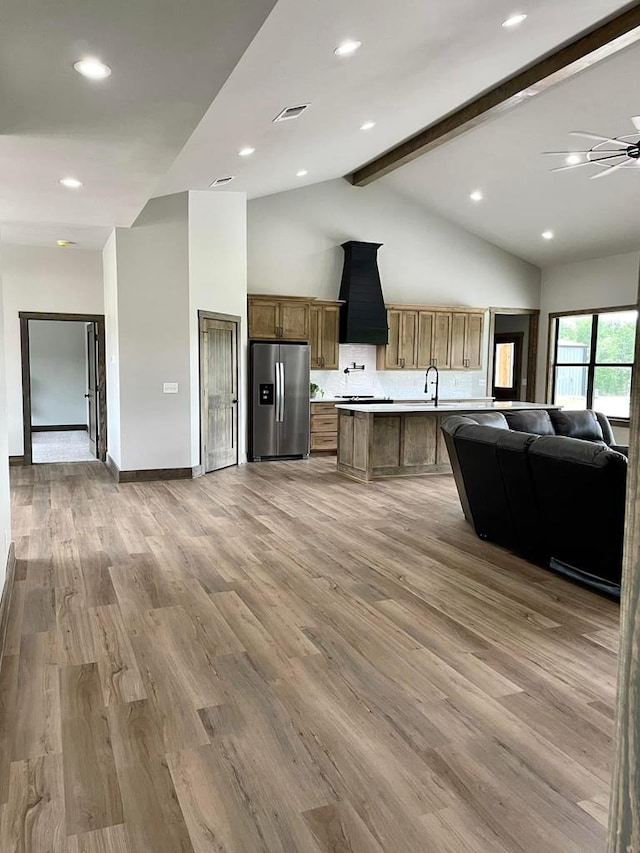 kitchen featuring open floor plan, light wood-style floors, stainless steel fridge, light countertops, and beam ceiling