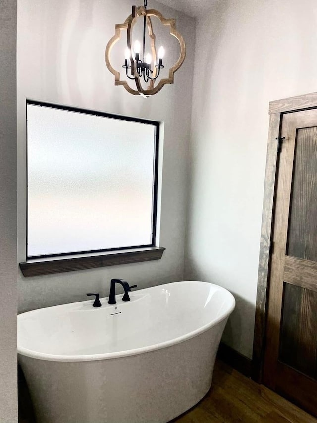 full bath with a notable chandelier, a freestanding tub, and wood finished floors