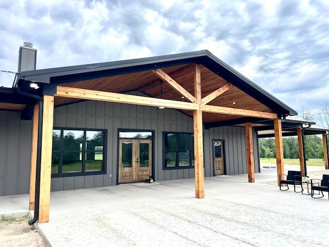 exterior space with board and batten siding, a chimney, and french doors