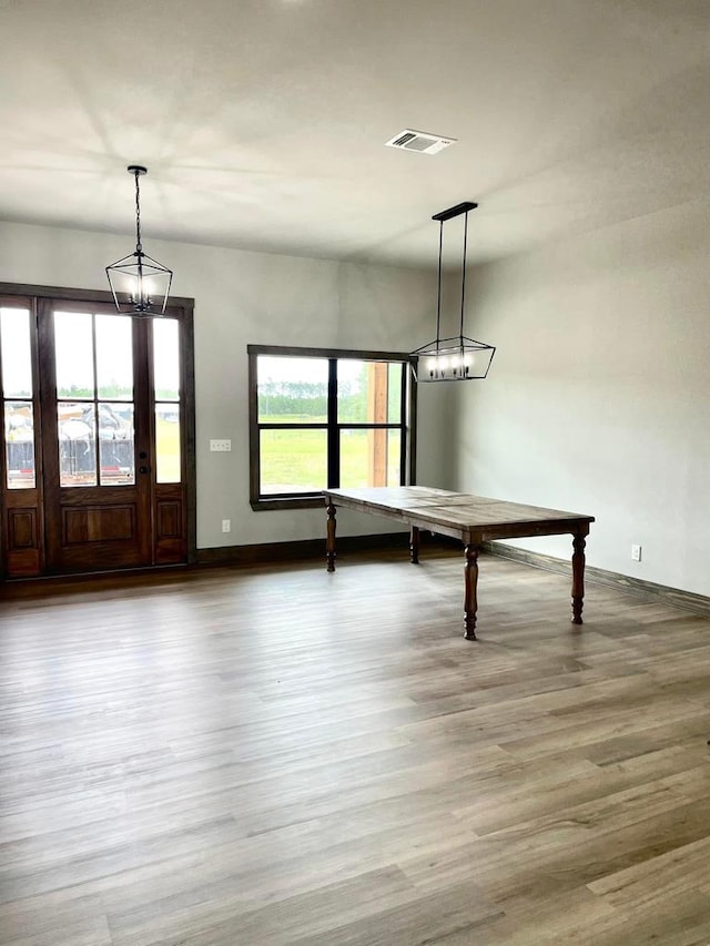unfurnished dining area featuring baseboards, wood finished floors, visible vents, and a chandelier