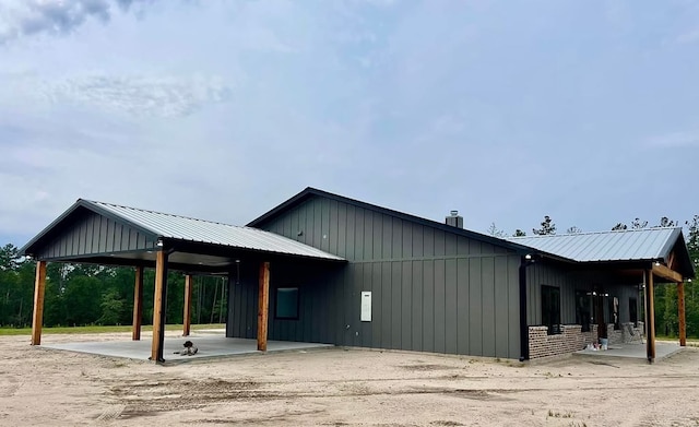 view of property exterior featuring board and batten siding, a chimney, a carport, and metal roof