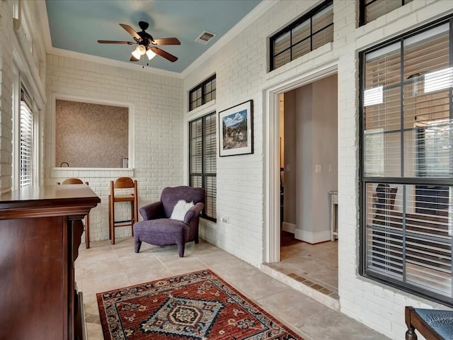 sitting room featuring ceiling fan, light tile patterned floors, ornamental molding, and brick wall