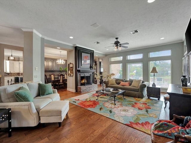 living room featuring a brick fireplace, light hardwood / wood-style flooring, ceiling fan, ornamental molding, and a textured ceiling