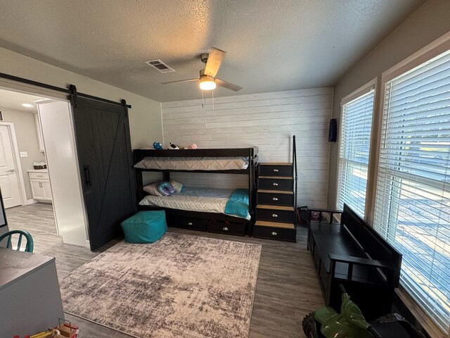 270 Lakeshore Dr, Brookeland, TX 75931 - bedroom featuring a barn door, a textured ceiling, dark wood-style flooring, wooden walls, and ceiling fan