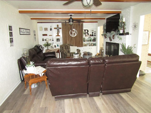 living room with a brick fireplace, ceiling fan, beamed ceiling, and light wood-type flooring