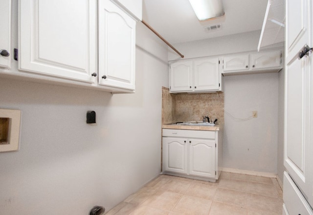 laundry room featuring cabinets, light tile patterned floors, and sink