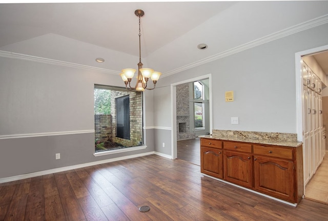 unfurnished dining area with a stone fireplace, crown molding, hardwood / wood-style floors, and a notable chandelier